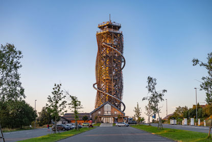 Blick über den Parkplatz zum hölzernen Turm mit Erlebnisrutsche und davorliegendem Eingangsgebäude