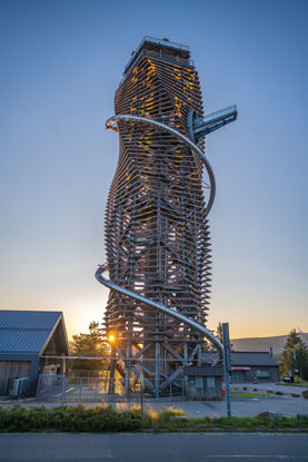hölzerner Turm mit Erlebnisrutsche und Skywalk im Sonnenuntergang, teilweise Blick auf angrenzendes Eingangsgebäude