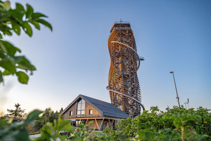 hölzerner Turm mit Erlebnisrutsche, Skywalk und Eingangsgebäude im Blick durch grüne Sträucher